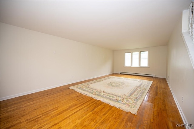 empty room with a baseboard radiator, light wood finished floors, and baseboards