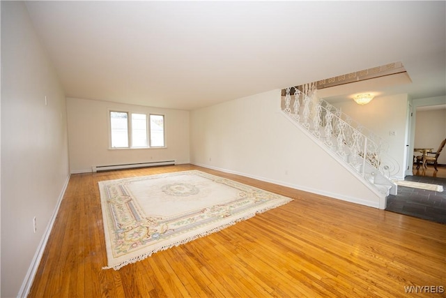 unfurnished living room featuring baseboard heating, stairs, wood finished floors, and baseboards