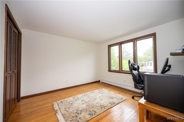 office area with a baseboard radiator, light wood-type flooring, and baseboards
