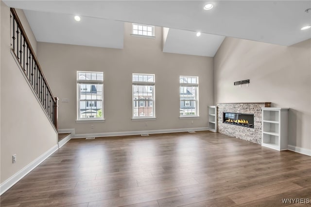 unfurnished living room featuring dark wood-style floors, baseboards, a towering ceiling, a fireplace, and stairs
