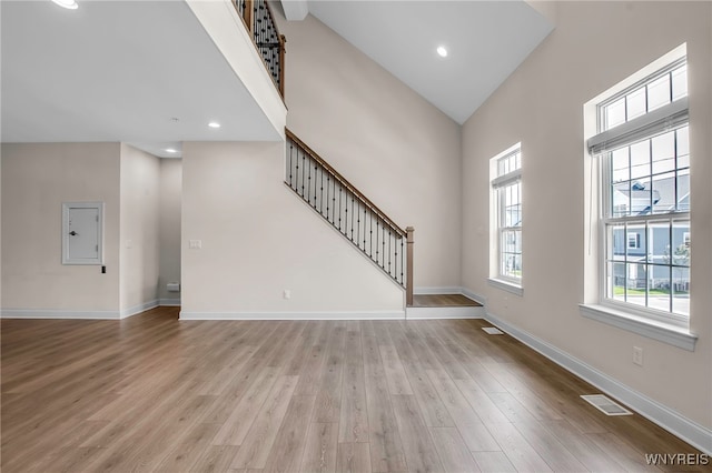 unfurnished living room with wood finished floors, baseboards, a towering ceiling, and recessed lighting