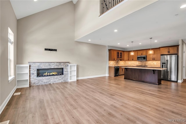 unfurnished living room with plenty of natural light, light wood-type flooring, a towering ceiling, baseboards, and recessed lighting