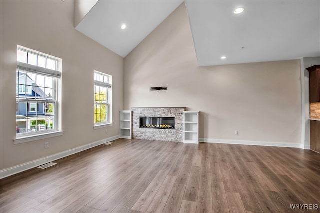 unfurnished living room with wood finished floors, a fireplace, high vaulted ceiling, baseboards, and recessed lighting