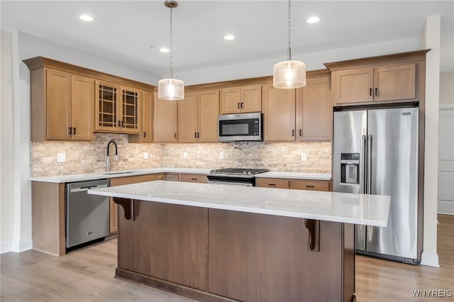 kitchen with appliances with stainless steel finishes, light wood-style floors, a sink, a kitchen island, and a breakfast bar area