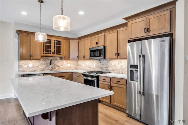 kitchen with stainless steel appliances, a sink, light wood-type flooring, light stone counters, and decorative light fixtures