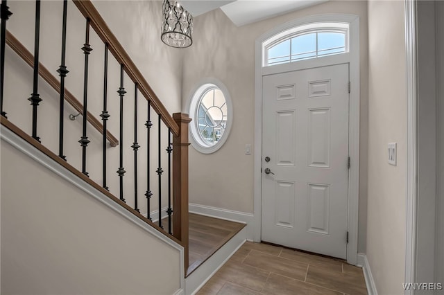 foyer entrance with healthy amount of natural light, a chandelier, stairway, and baseboards