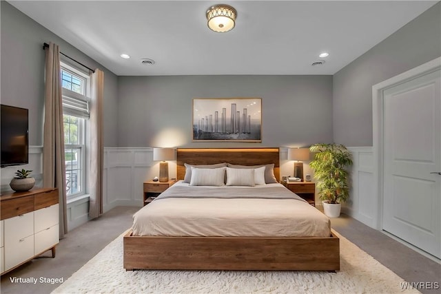 bedroom with a wainscoted wall, light colored carpet, a decorative wall, and recessed lighting