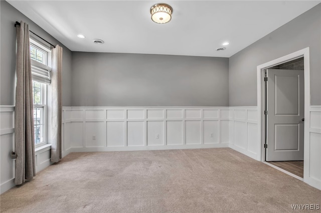 empty room featuring a decorative wall, light carpet, wainscoting, and recessed lighting