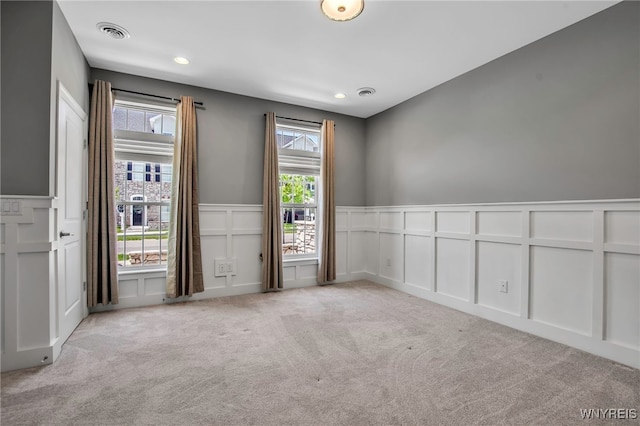 empty room with a decorative wall, light carpet, wainscoting, and recessed lighting