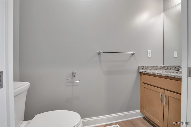 bathroom featuring toilet, vanity, wood finished floors, and baseboards