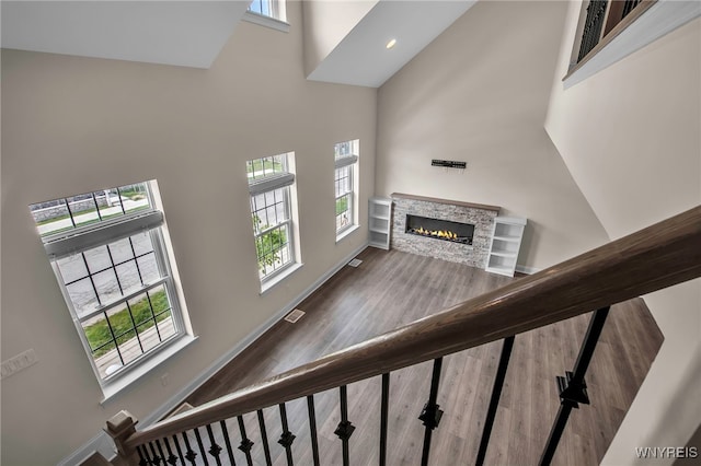 stairway featuring a towering ceiling, a stone fireplace, wood finished floors, healthy amount of natural light, and baseboards