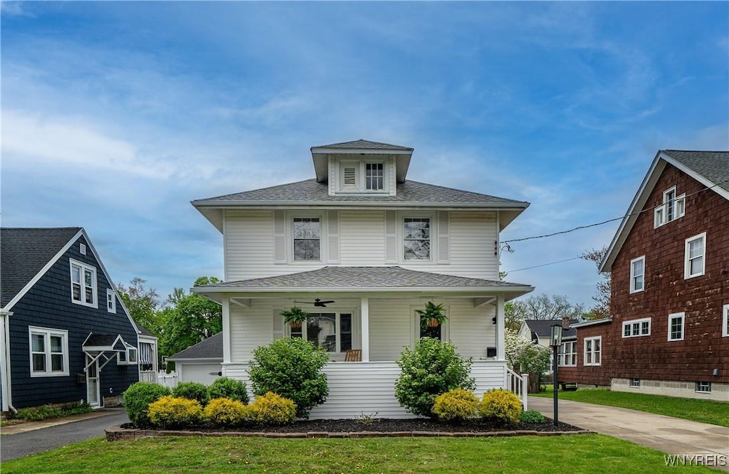 american foursquare style home featuring covered porch, roof with shingles, and a front yard