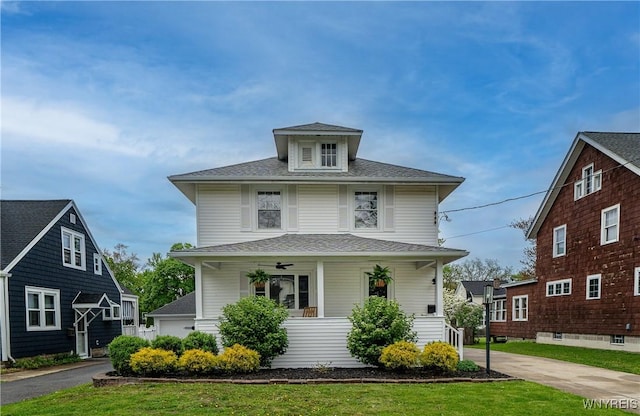american foursquare style home featuring covered porch, roof with shingles, and a front yard