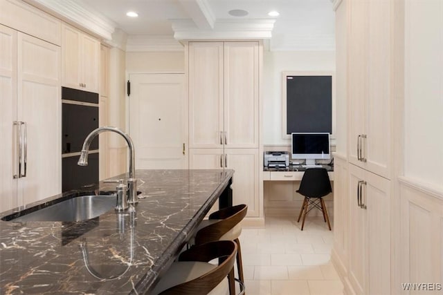 kitchen featuring a sink, a kitchen breakfast bar, ornamental molding, dark stone countertops, and light tile patterned floors