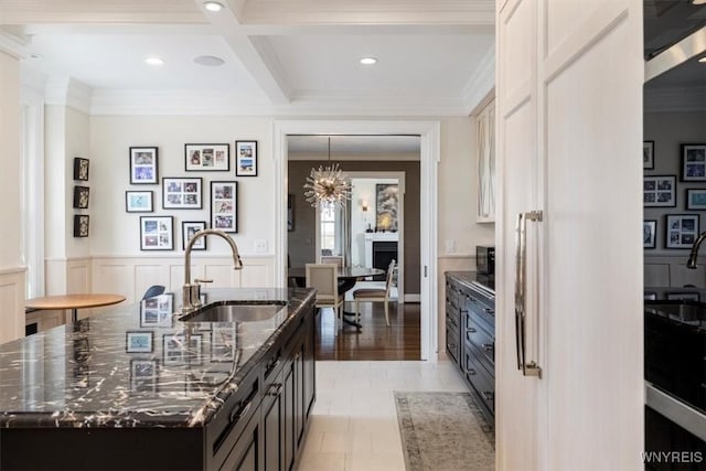 kitchen with a sink, crown molding, beamed ceiling, dark stone countertops, and coffered ceiling