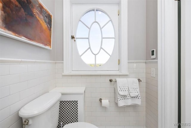 half bath with toilet, tile walls, and a wainscoted wall