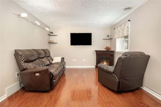 living room featuring a textured ceiling, wood finished floors, a warm lit fireplace, and baseboards