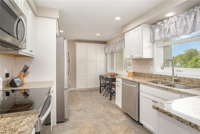 kitchen featuring appliances with stainless steel finishes, a sink, white cabinets, recessed lighting, and light stone counters