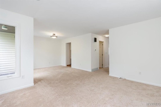 spare room featuring light carpet and baseboards
