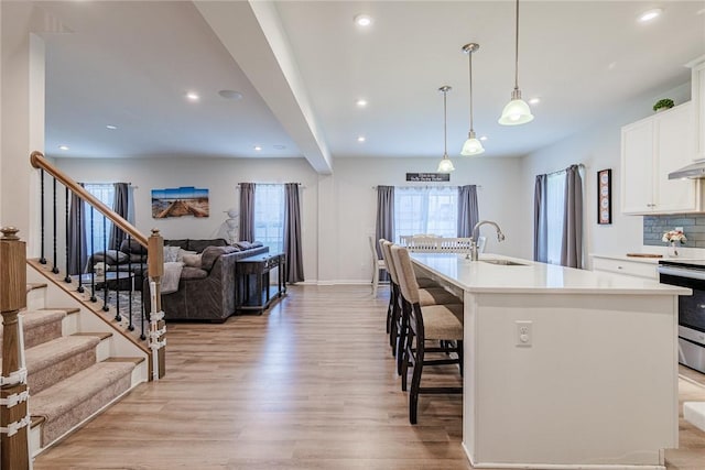 kitchen with a sink, electric stove, open floor plan, light wood-type flooring, and white cabinets