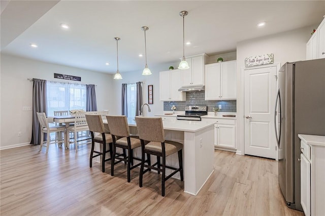 kitchen featuring appliances with stainless steel finishes, under cabinet range hood, light wood-type flooring, backsplash, and light countertops