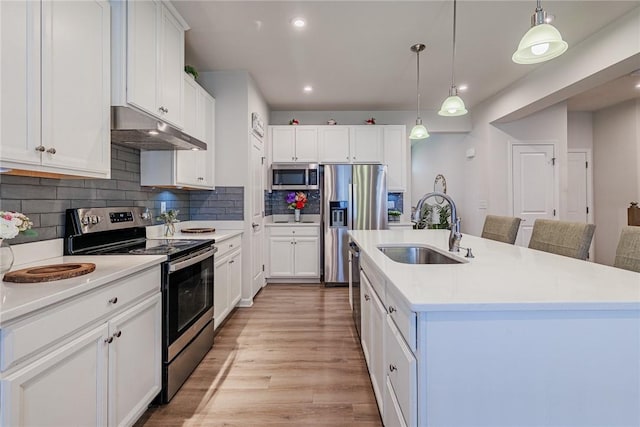 kitchen with stainless steel appliances, under cabinet range hood, a sink, light countertops, and tasteful backsplash