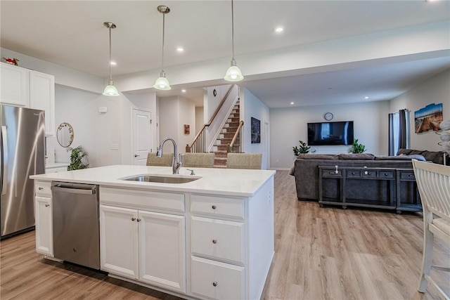 kitchen featuring appliances with stainless steel finishes, a sink, light wood finished floors, open floor plan, and light countertops