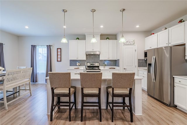kitchen with appliances with stainless steel finishes, light countertops, decorative backsplash, a kitchen bar, and recessed lighting