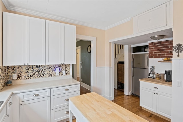 kitchen featuring freestanding refrigerator, white cabinets, crown molding, decorative backsplash, and wood finished floors