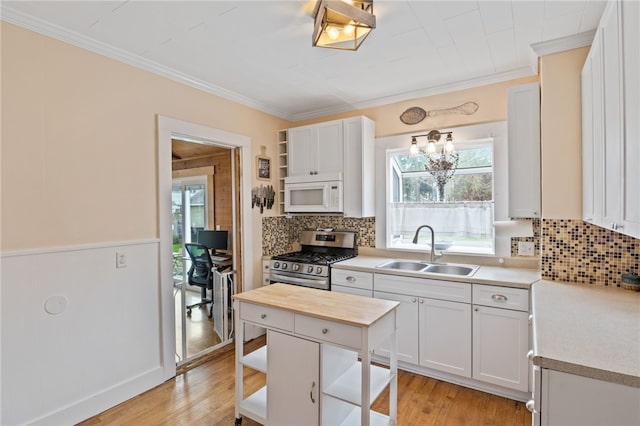kitchen featuring stainless steel range with gas stovetop, white microwave, a sink, open shelves, and butcher block countertops