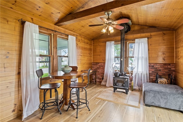 dining room with a wood stove, wood walls, light wood-type flooring, a ceiling fan, and wooden ceiling