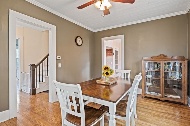 dining room featuring ceiling fan, light wood finished floors, ornamental molding, and stairway