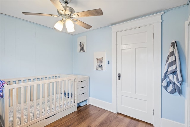 bedroom with wood finished floors, baseboards, a crib, and ceiling fan