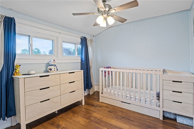 bedroom with dark wood finished floors, lofted ceiling, ceiling fan, and a nursery area