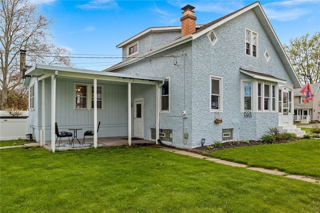 rear view of property featuring a chimney, a yard, and a patio