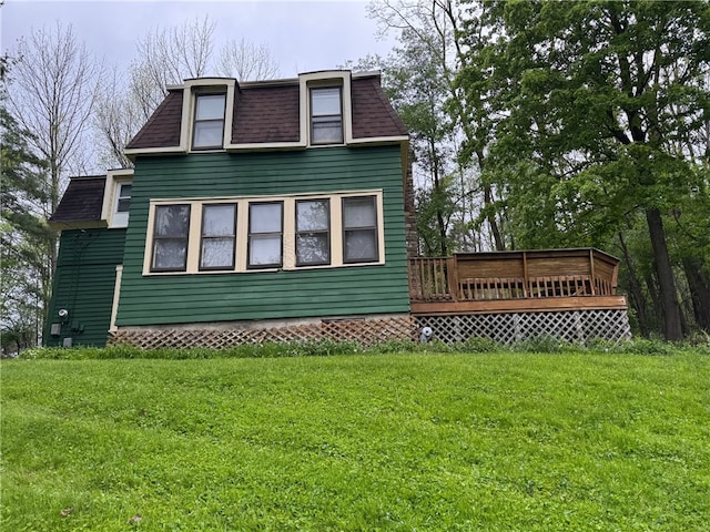 view of front facade with a wooden deck, roof with shingles, a front yard, and mansard roof