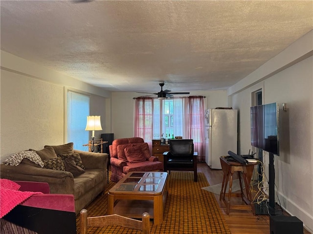 living area with a textured ceiling, wood finished floors, a textured wall, and ceiling fan