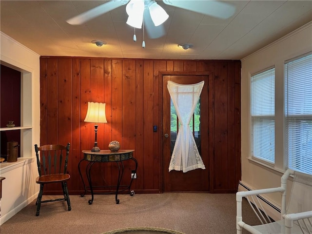 living area featuring carpet flooring, wood walls, ceiling fan, ornamental molding, and baseboard heating