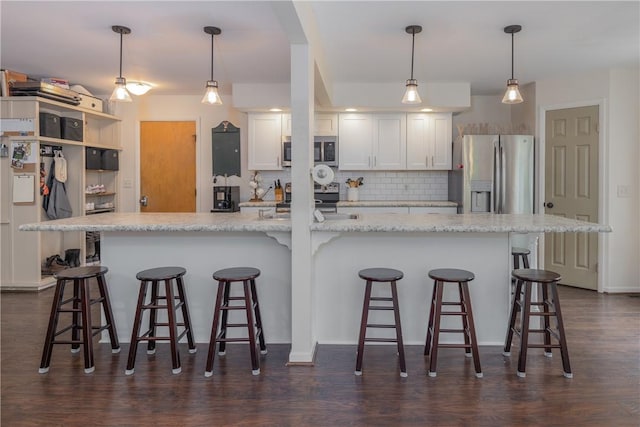 kitchen featuring appliances with stainless steel finishes, backsplash, white cabinetry, and a breakfast bar area