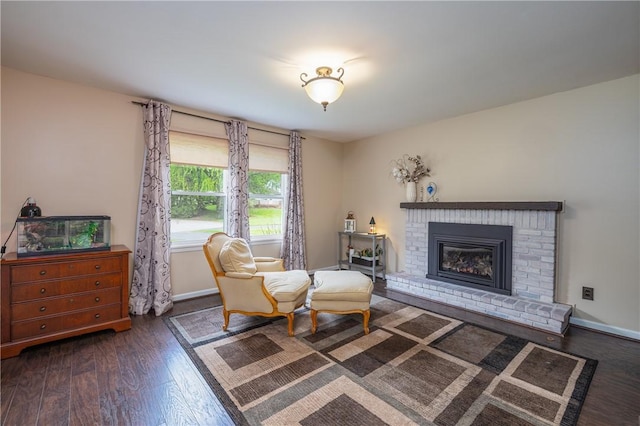 living area featuring wood finished floors, baseboards, and a brick fireplace