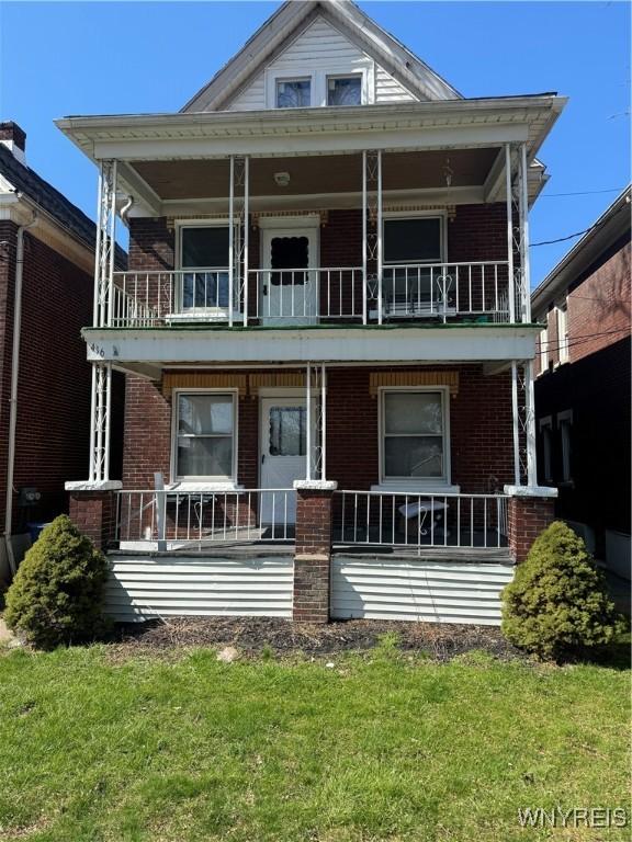 rear view of property featuring a balcony, covered porch, brick siding, and a lawn