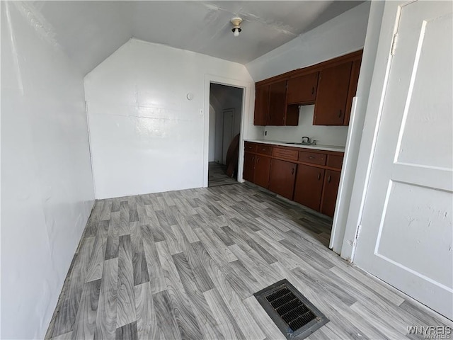 kitchen featuring a sink, light countertops, lofted ceiling, and light wood finished floors