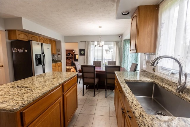 401 Montvale Ln, Greece, NY 14626 - kitchen with stainless steel fridge, a sink, brown cabinets, a chandelier, and light stone counters