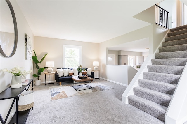 living room featuring carpet, baseboards, and stairs