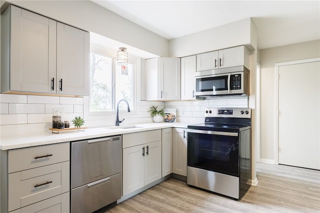 kitchen with stainless steel appliances, a sink, decorative backsplash, light wood-type flooring, and light countertops