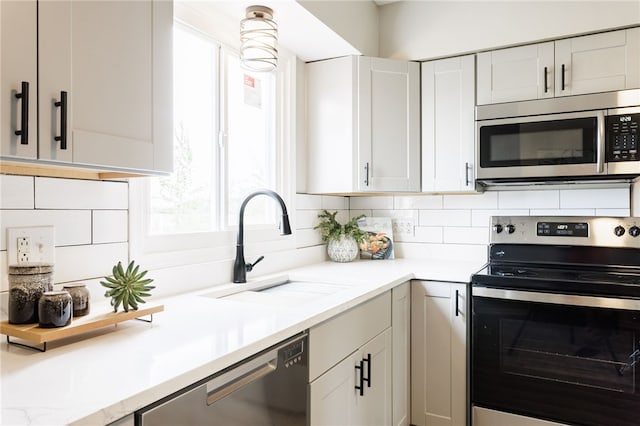 kitchen featuring stainless steel appliances, a sink, tasteful backsplash, and white cabinetry