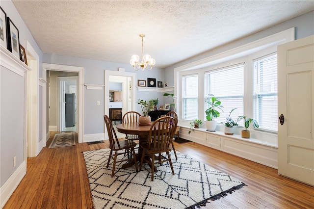 dining area with a chandelier, light wood finished floors, a textured ceiling, and baseboards