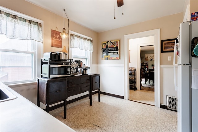 kitchen with plenty of natural light, stainless steel microwave, a wainscoted wall, freestanding refrigerator, and ceiling fan