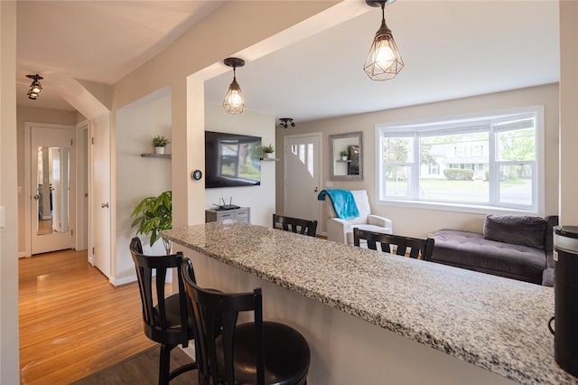 kitchen featuring a kitchen bar, light wood finished floors, light stone countertops, and hanging light fixtures