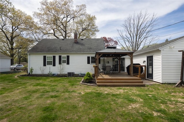 rear view of house with a gazebo, a wooden deck, a lawn, and a chimney